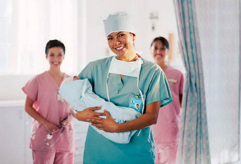 Delivery room nurse holding baby, nurses in background